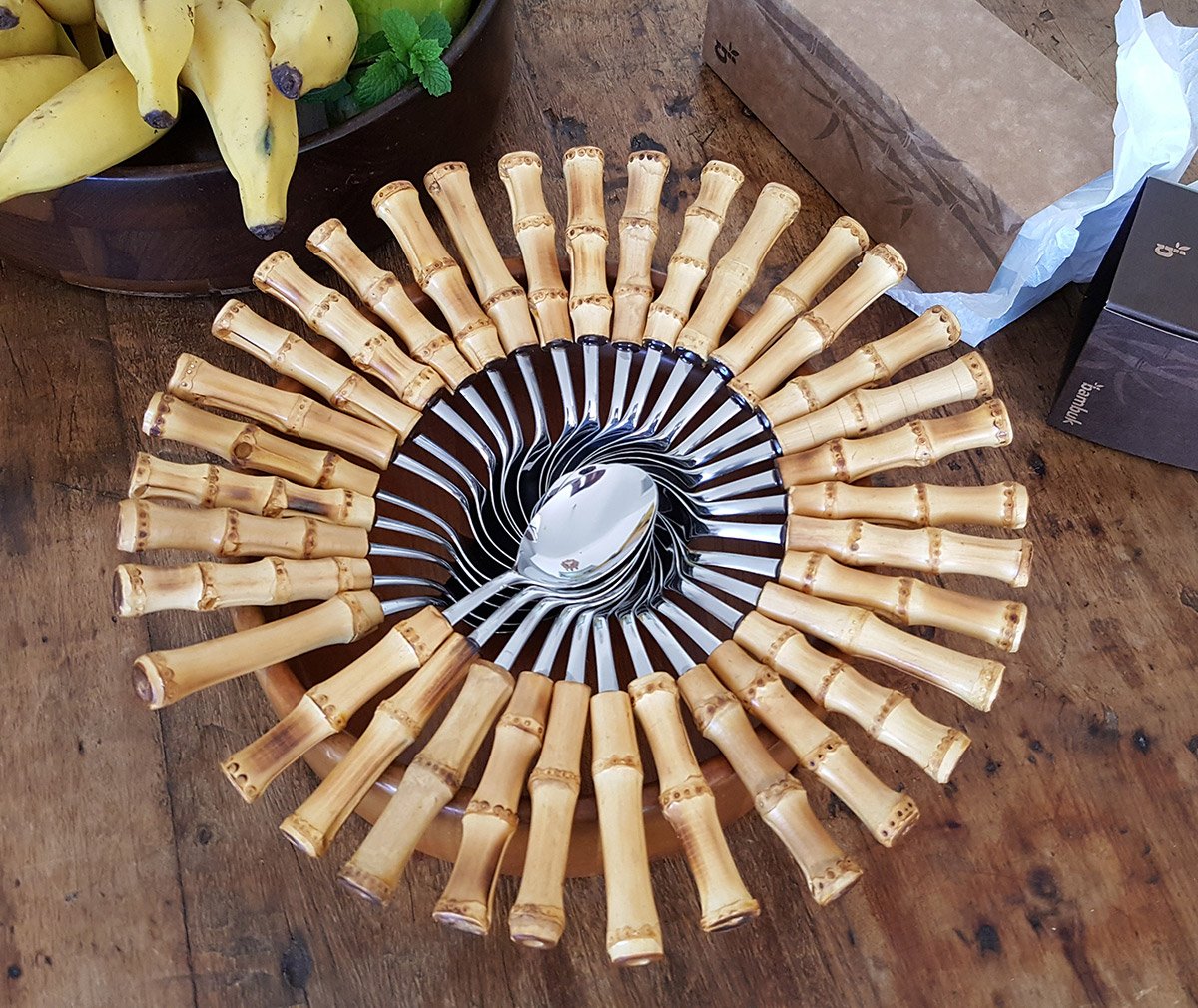 colhers de inox da tramontina com cabo de bambu natural colocadas em forma de caracol sob uma mesa elgante e rustica de madeira